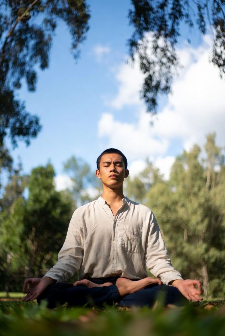 A high-resolution, slightly blurred photorealistic image of a person meditating cross-legged in a lush forest clearing at dusk,
