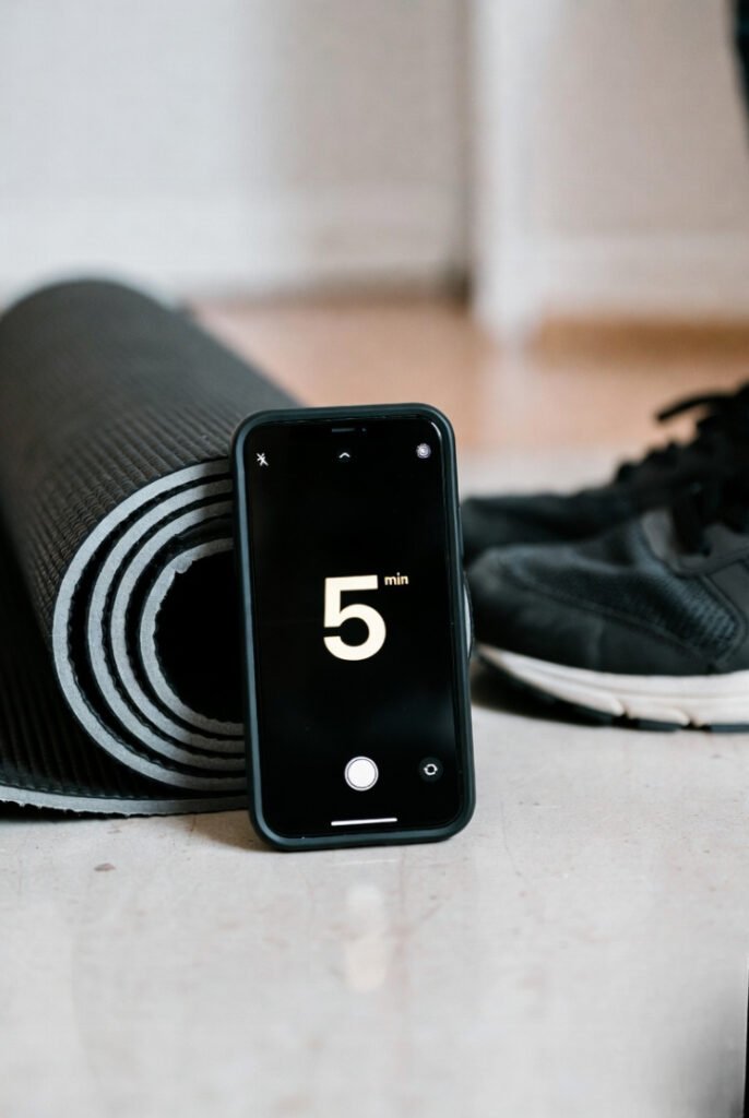 Close-up of a phone timer set to 5 minutes next to a yoga mat and sneakers, soft indoor lighting.