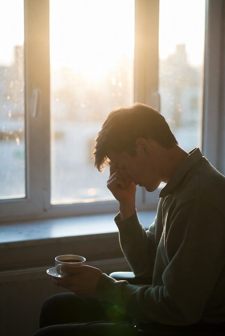 Here's a short alt text (under 10 words): **Man enjoying morning tea by the window in soft sunlight.**